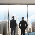 Two Envisage Law lawyers looking out a wall of windows onto the Raleigh skyline